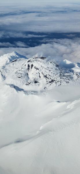 A view of Great Sitkin's summit crater and lava activity, taken from an Alaska airlines flight departing Adak for Anchorage. Some steaming and bare ground are visible where the flow is warm.