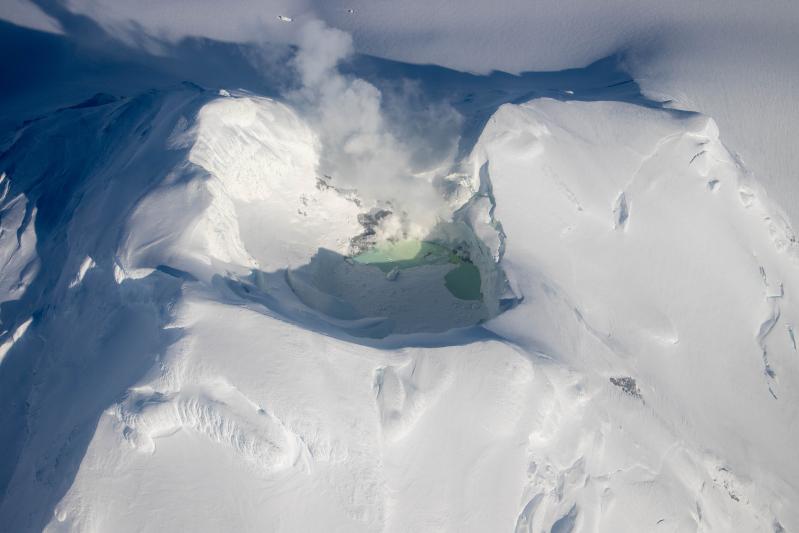 Lake inside of the Mount Spurr summit crater with fumaroles and discolored water on March 21, 2025. Much of the lake surface is covered in snow and ice.