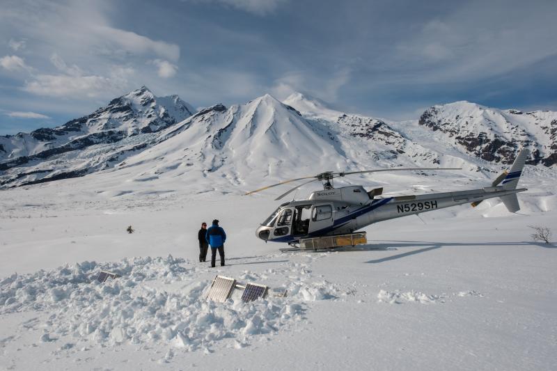 AVO field crews working at clearing AVO monitoring sit SPCN with Crater Peak and Mount Spurr in the background. The hut and solar panels were dug out from snow to improve power and radio telemetry from the site. 