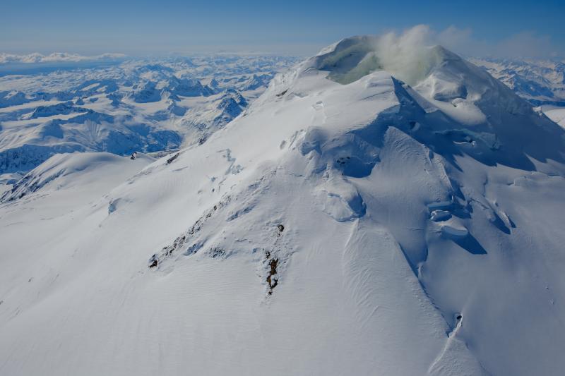 View of the northeast flank of the Mount Spurr summit cone on April 25 during an AVO gas and photo survey. Steam and gas emissions are visible from the summit crater. A snowless patch in the center of the image is a long-lived warm area on the flank of the upper cone. Crater Peak is just visible in the center left of the image.