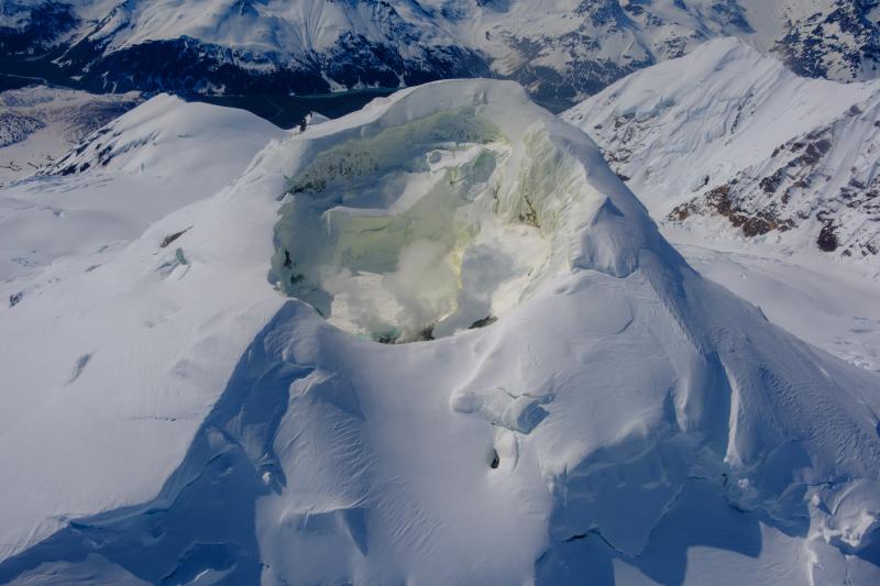 Mount Spurr summit from the north during a gas and photo survey on June 11, 2025. Sulfur has stained the snow yellow within the summit crater. Fumaroles are producing a light steam plume from the north shore of the crater lake. Crater Peak is just visible in the background to the left of the summit crater.