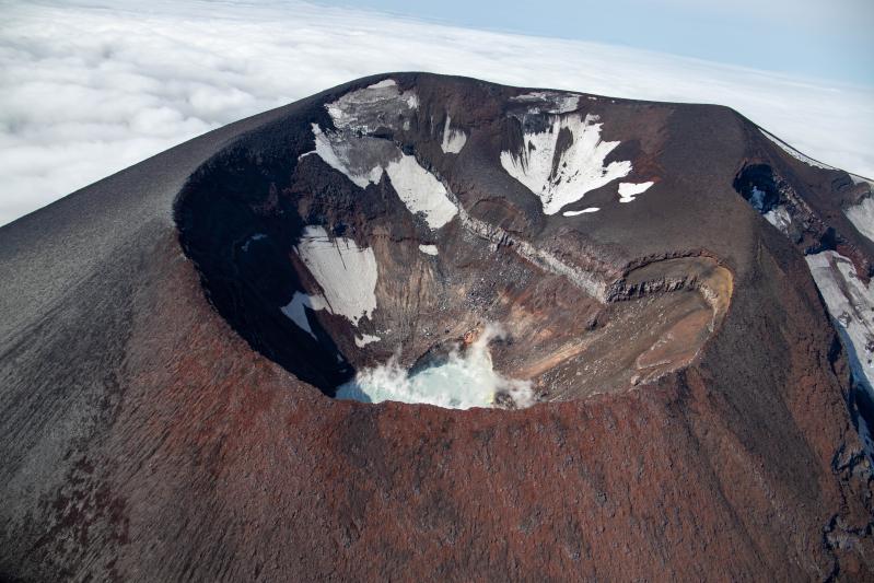 Summit crater and crater lake at Korovin Volcano in the Atka Volcanic Complex during an Alaska Volcano Observatory observation and gas measurement flight on August 28, 2025. The lake is warm with sulfur deposits floating on top due to an active hydrothermal system.
