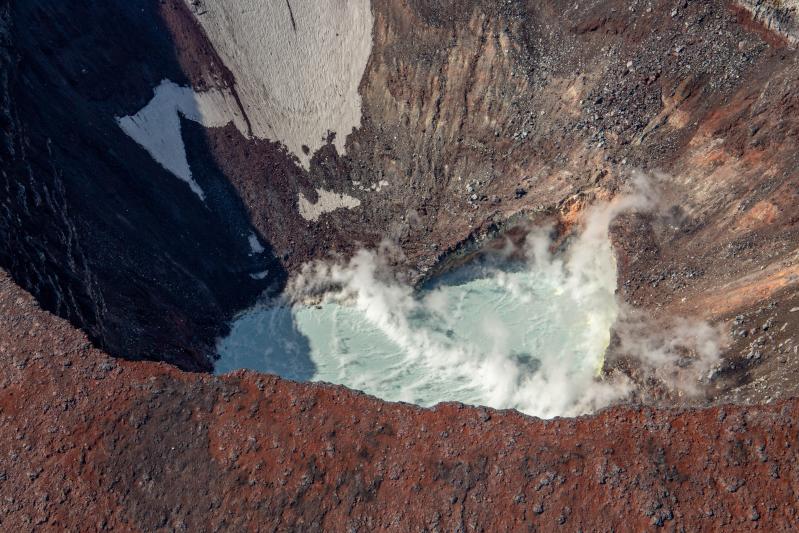 Steaming crater lake inside of the summit crater of Korovin Volcano in the Atka Volcanic Complex during an Alaska Volcano Observatory observation and gas measurement flight on August 28, 2025. The lake is warm with sulfur deposits floating on top due to an active hydrothermal system.
