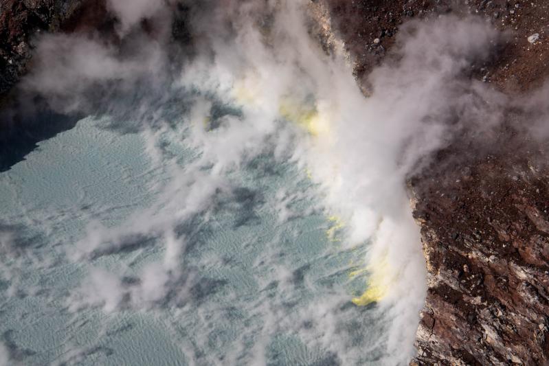 Steaming crater lake inside of the summit crater of Korovin Volcano in the Atka Volcanic Complex during an Alaska Volcano Observatory observation and gas measurement flight on August 28, 2025. The lake is warm with yellow sulfur deposits floating on top due to an active hydrothermal system.