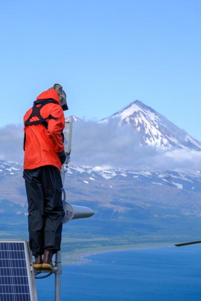 AVO field engineer Mitch Mitchell adjusting the Dolgoi Island webcam, with Pavlof Volcano visible in the background. 