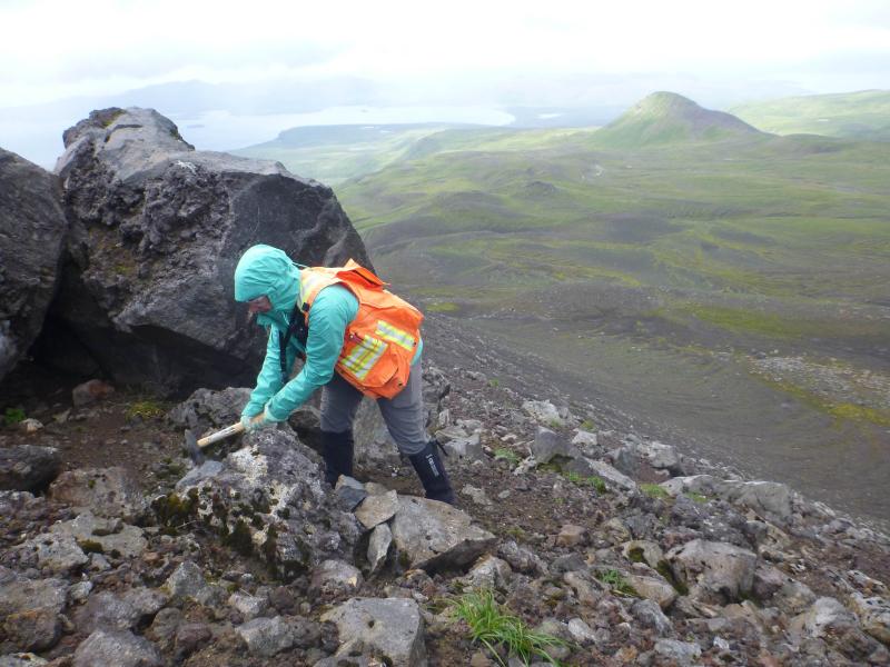 USGS geologist Hannah Dietterich collecting a Pleistocene lava sample from the south flank of Kliuchef volcano. Photo taken during field work at Atka volcanic complex, northern Atka Island. 