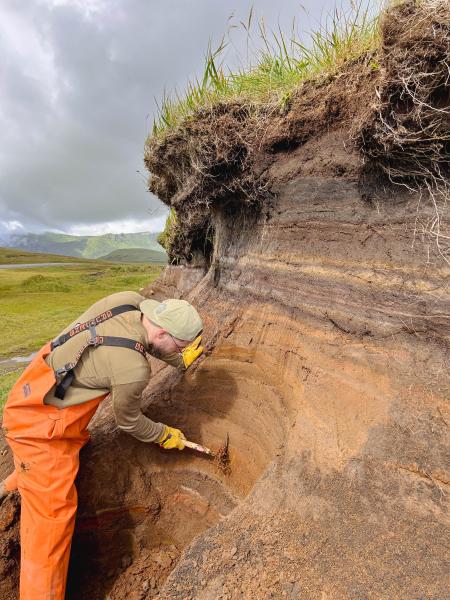 USGS geologist Jordan Lubbers cleaning off tephra section near Atka airport (25AAHD001). Photo taken during field work at Atka volcanic complex, northern Atka Island. 