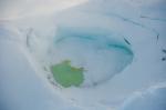 Summit crater of Mount Spurr with a partially ice-covered crater lake on December 18, 2024. Yellow sulfur precipitates are visible floating on the surface. Photo taken part of a photo and gas survey following recent seismic unrest at the volcano.