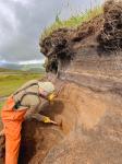 USGS geologist Jordan Lubbers cleaning off tephra section near Atka airport (25AAHD001). Photo taken during field work at Atka volcanic complex, northern Atka Island. 